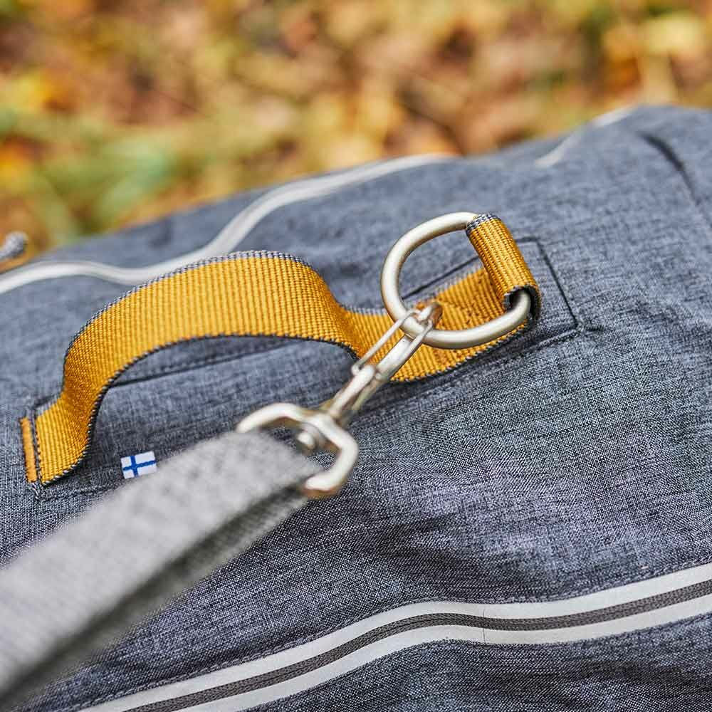 Close-up of a blue backpack with a yellow strap and metal buckle, set against a blurred natural background.